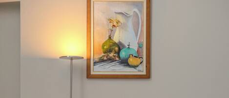 A room with a brown leather sofa, a floor lamp, and a framed artwork on the wall.