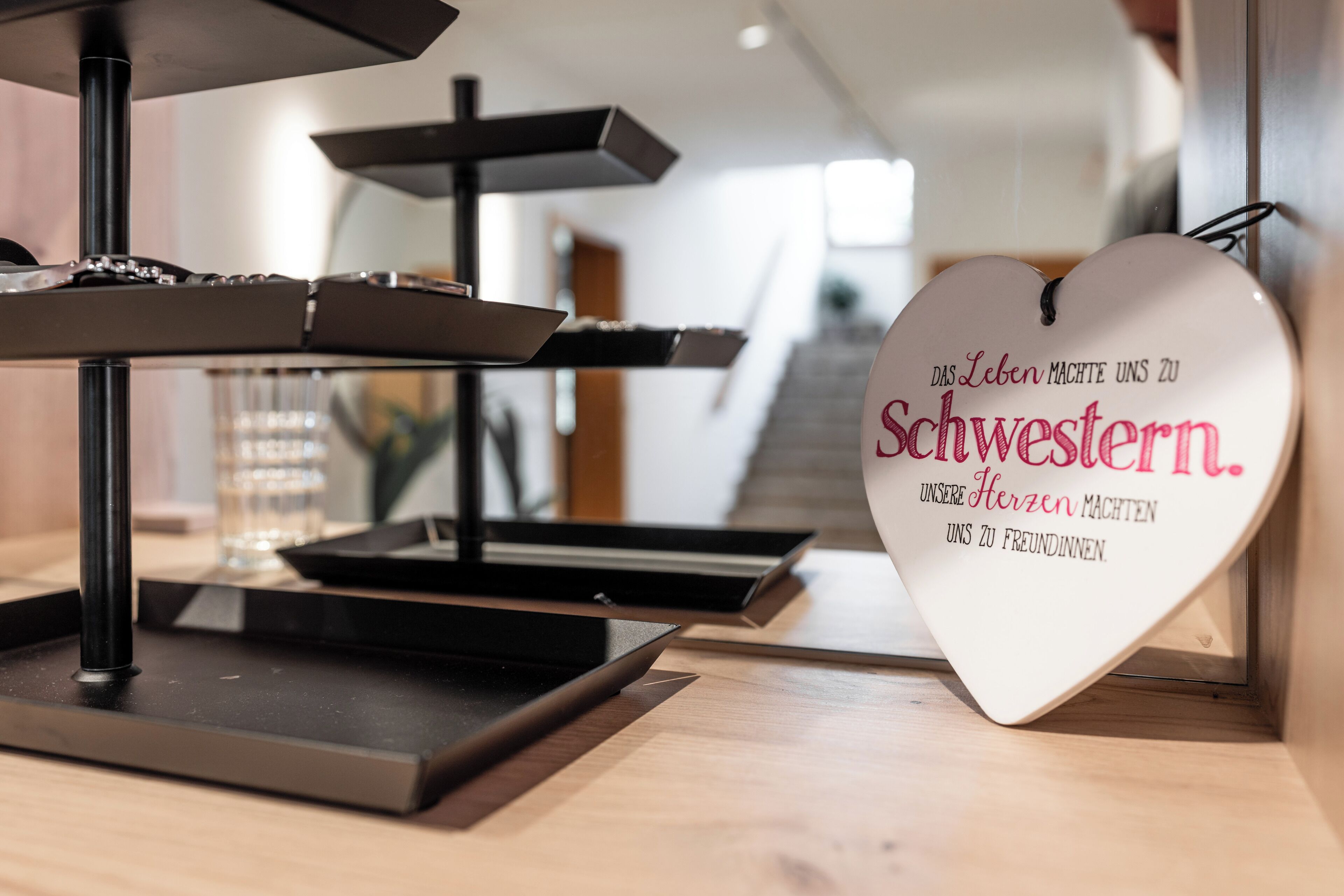 A heart-shaped sign with text in a foreign language, a black metal stand, and a wooden surface.