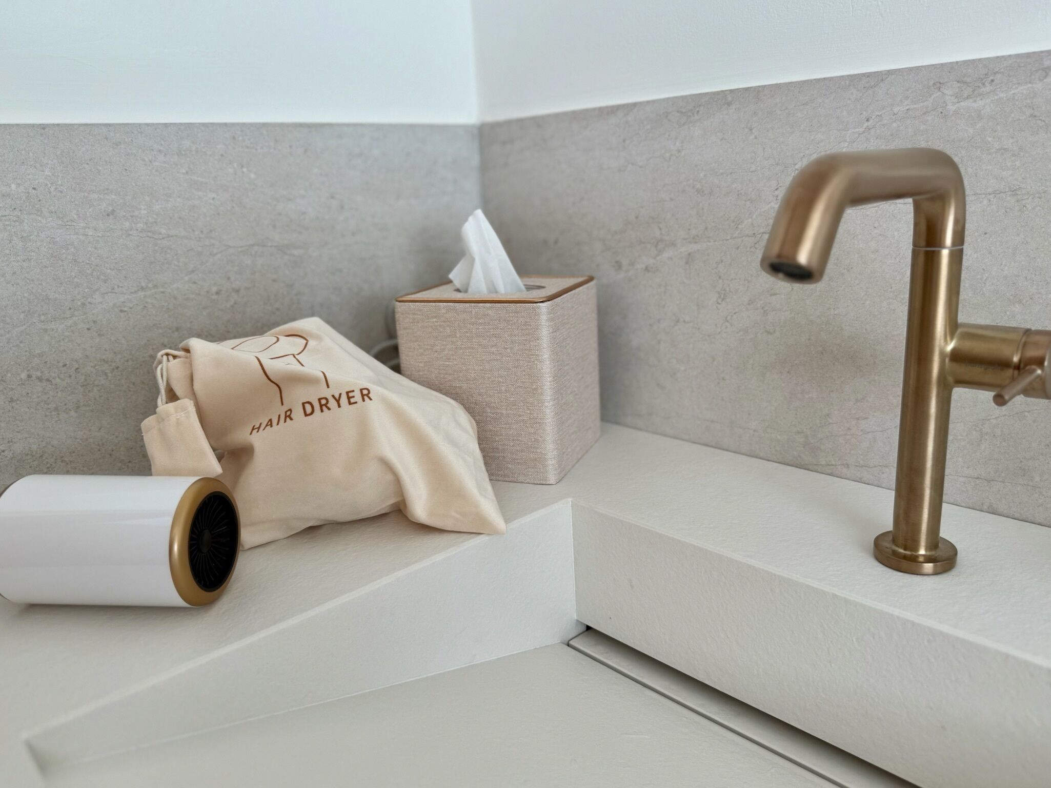 Een badkamer met een handdoek, zakdoekjes en een haardroger op een witte plank.