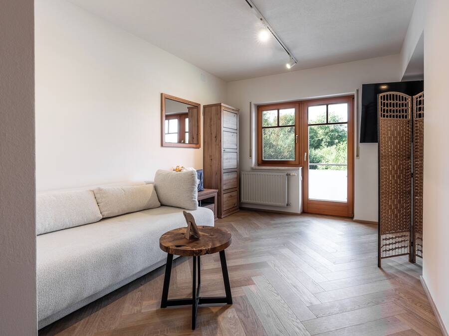 Una sala moderna con un sofá, una mesita de madera, un radiador y una ventana con vistas a zonas verdes.