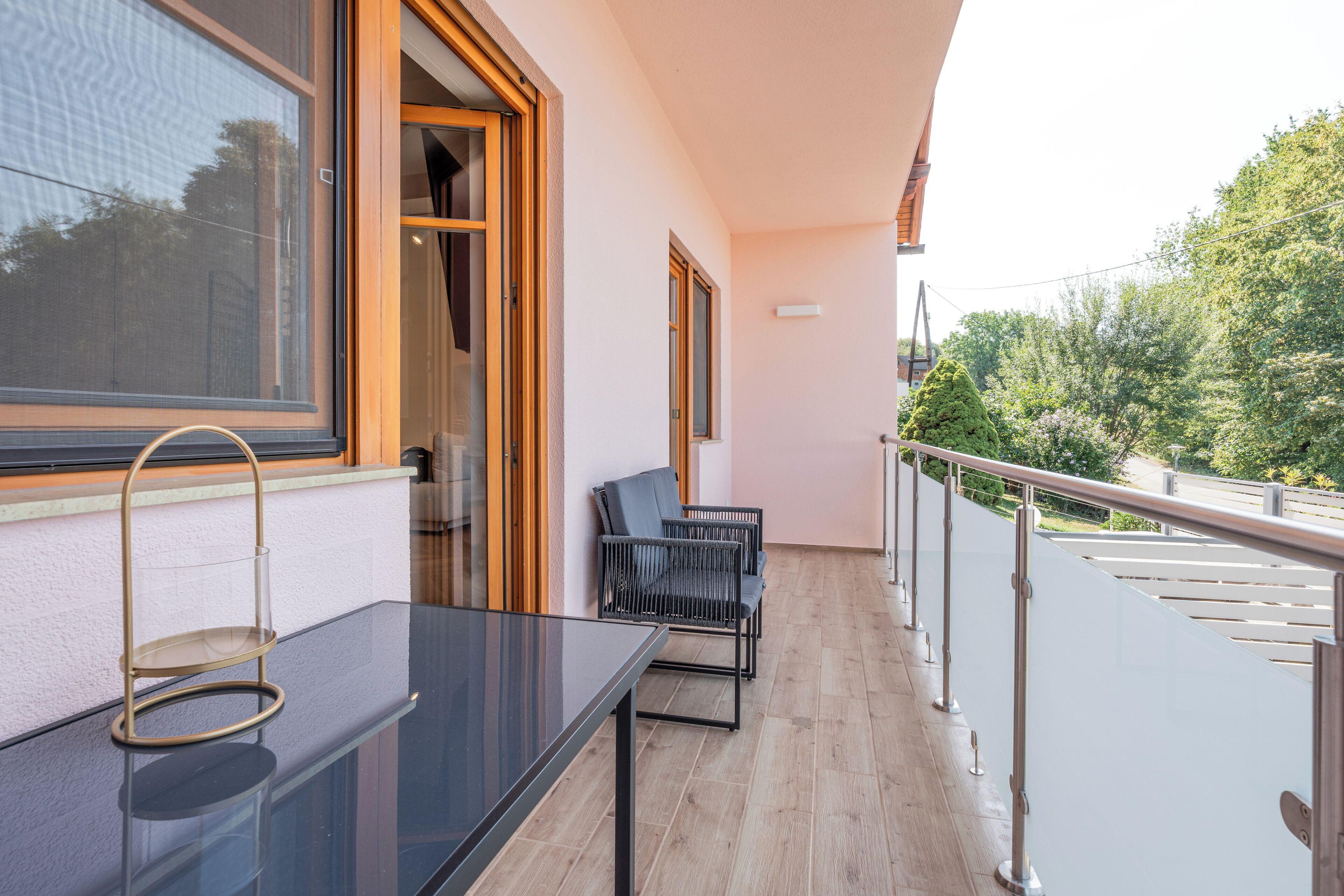 A balcony with a glass table, two chairs, and a wooden railing.