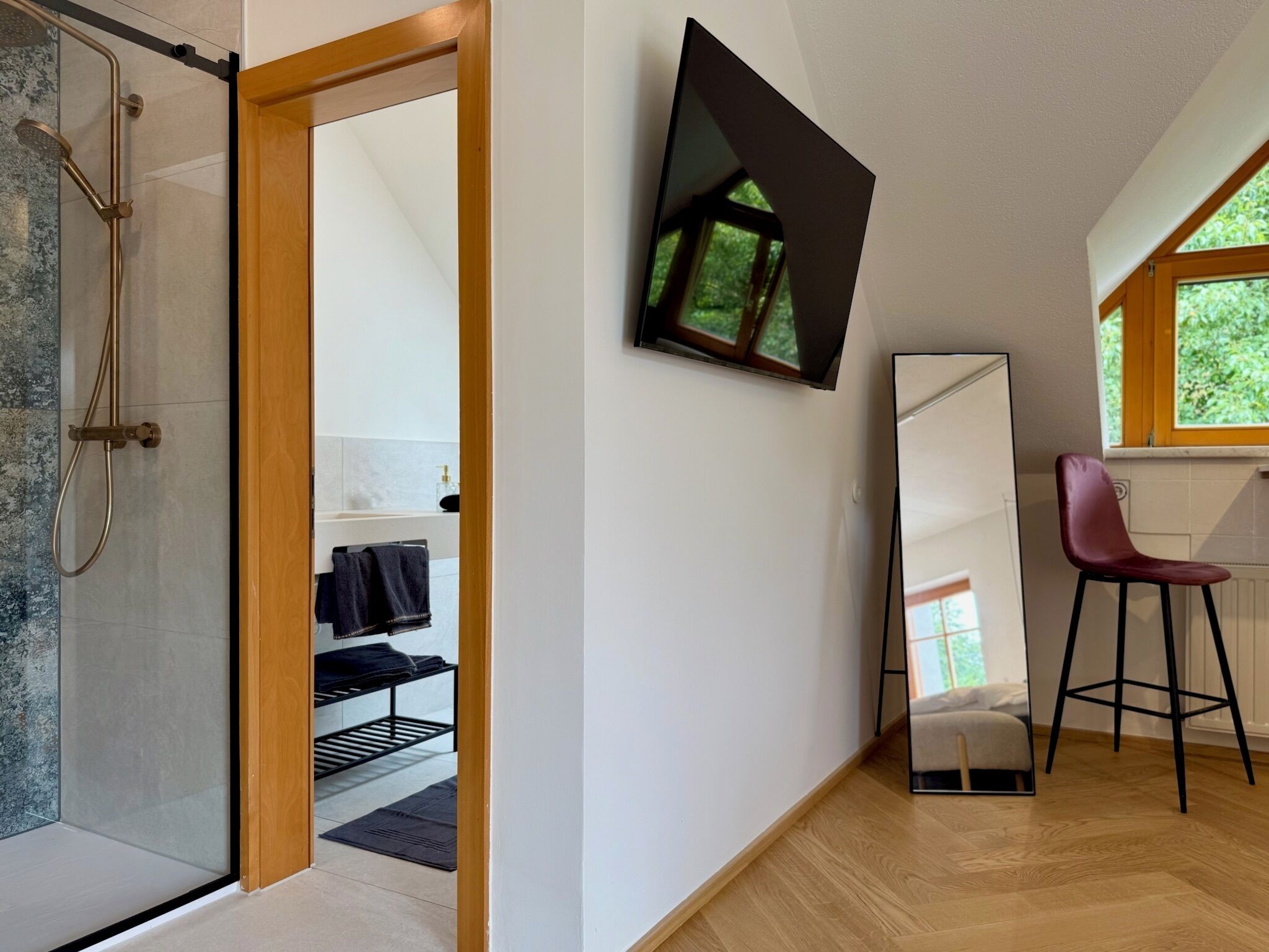 A modern bathroom with a glass shower enclosure, a wooden door, a towel rack, and a mirror.