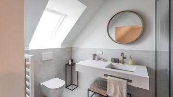 A modern bathroom with a skylight, a round mirror, a white sink, and a towel rack.
