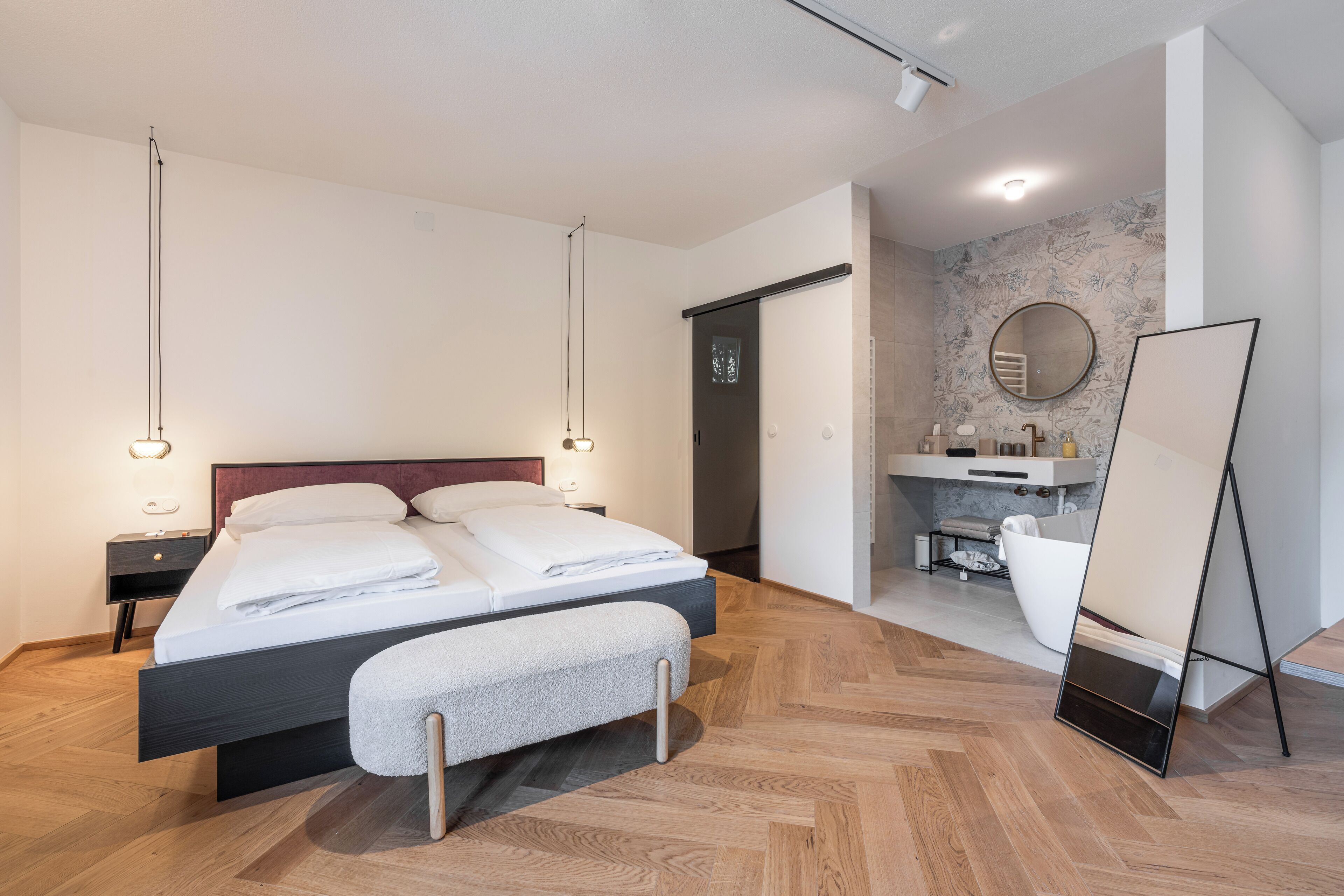 A modern bedroom with a large bed, bedside tables, a mirror, and a bathroom visible through an open door.