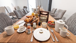 Un desayuno servido en una mesa de madera, con diversas opciones y en una habitación moderna con sillas tapizadas en gris.