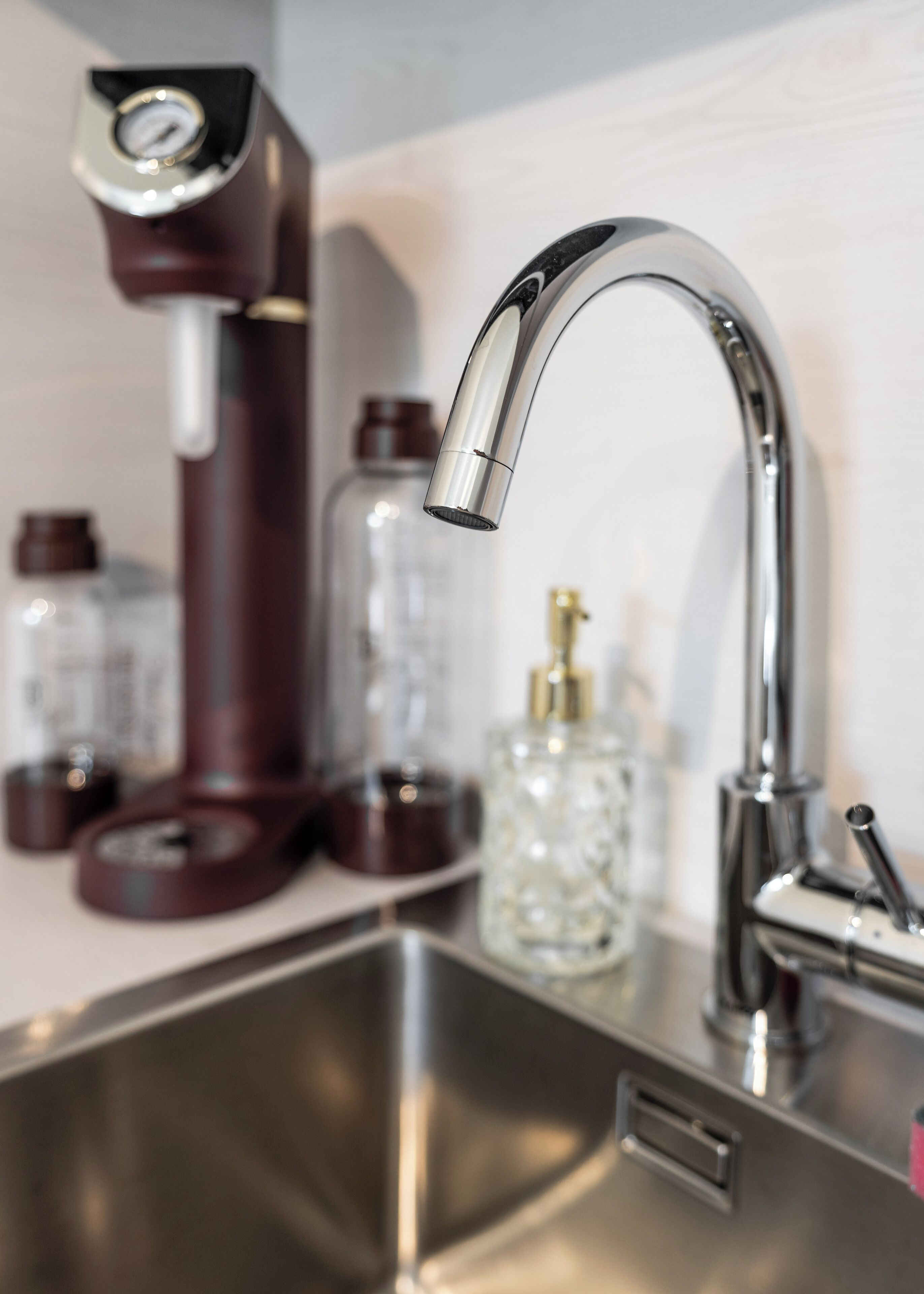 A kitchen sink with a modern faucet, a coffee maker, and a glass container on the counter.
