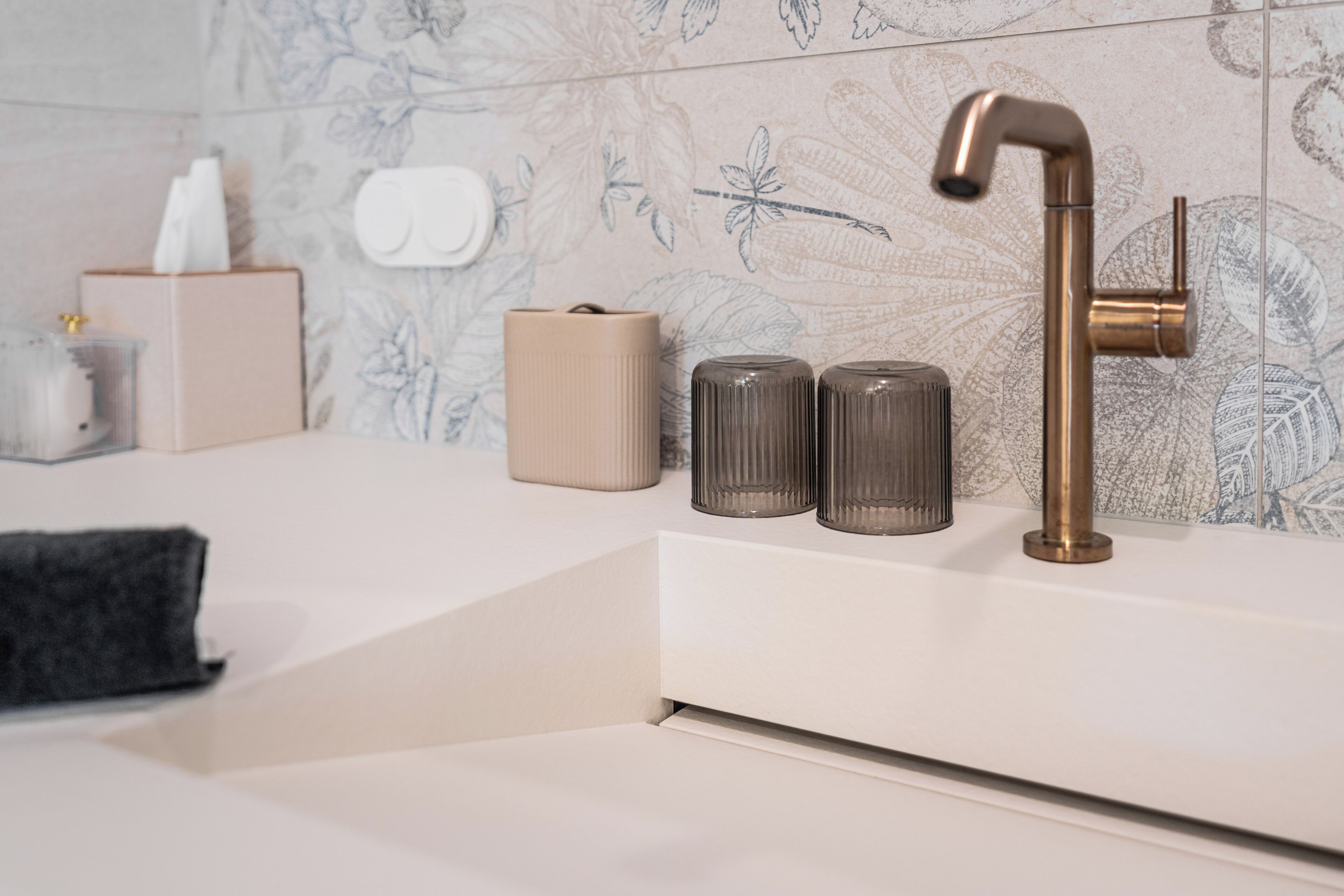 A bathroom with a modern faucet, a tissue box, and two glass containers on the counter.