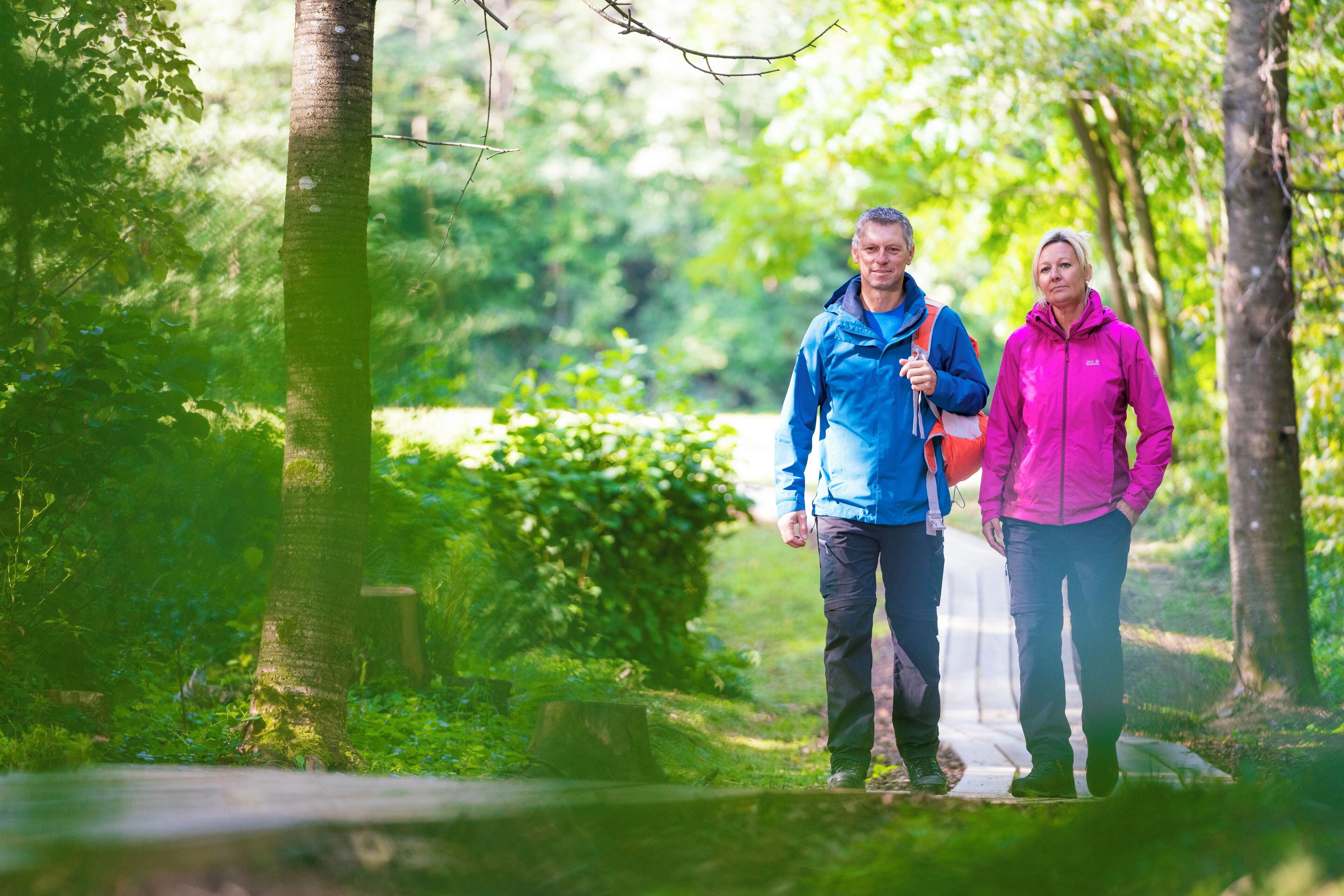Two people walking on a path in a green, wooded area.