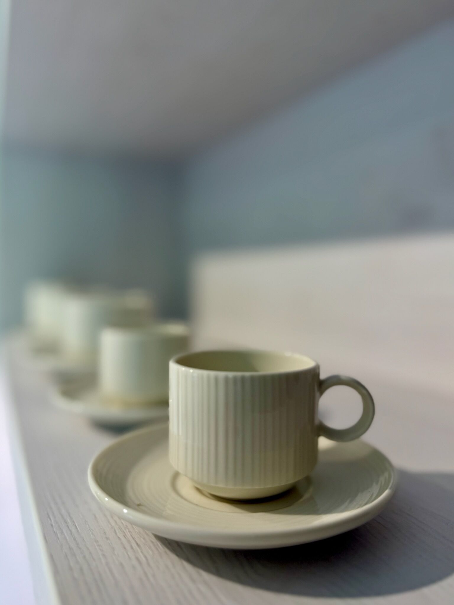 A white ceramic cup and saucer on a white surface, with a blurred background.