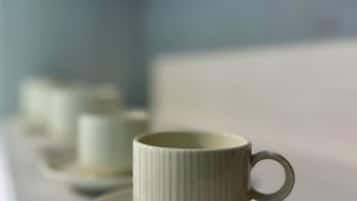 A white ceramic cup and saucer on a white surface, with a blurred background.