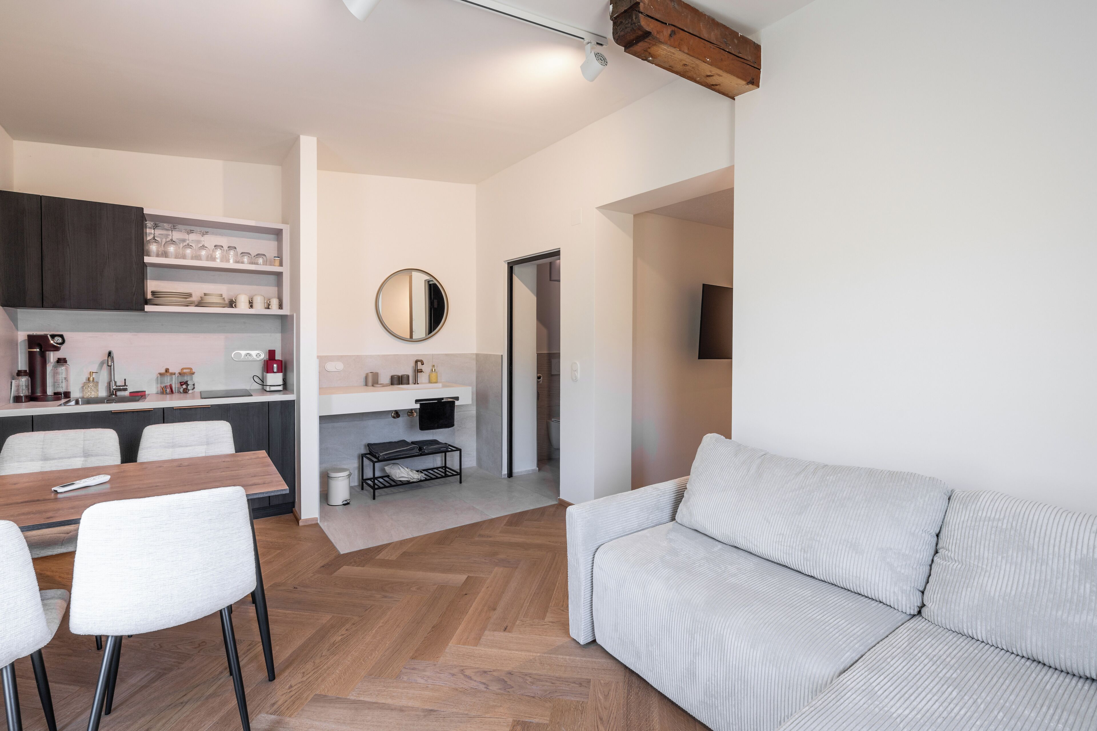 Una sala de estar moderna con un sofá, una mesa de comedor con sillas, una zona de cocina con armarios y un lavabo, y un espejo en la pared.