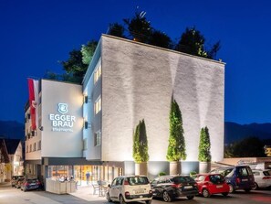 A hotel with a modern facade, a visible entrance, and a parking area with several cars.