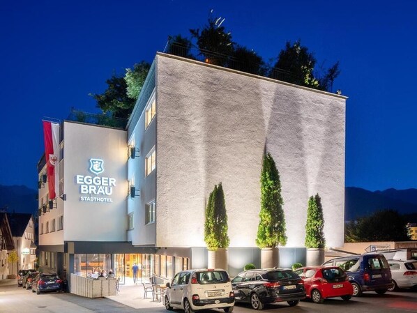 A hotel with a modern facade, a visible entrance, and a parking area with several cars.