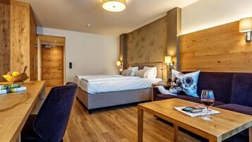 Una habitación de hotel moderna con una pared de acento de madera, una cama con ropa de cama blanca, un sofá, una mesa de centro de madera y un escritorio con una silla.