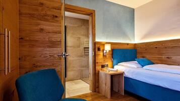 Una habitación con un armario de madera, una cama con ropa de cama azul, una mesita de noche con una lámpara y una silla.