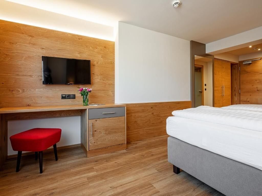 Una habitación de hotel moderna con una pared de acento de madera, un televisor de pantalla plana, un escritorio con silla, una cama y un armario.