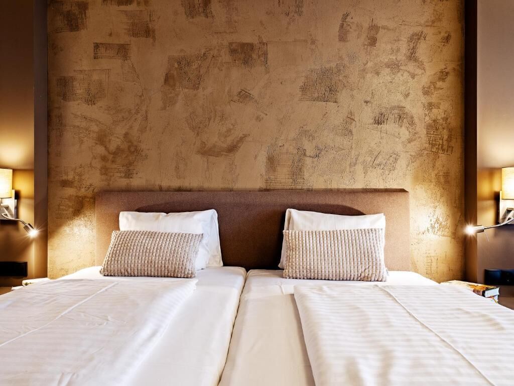 A double bed with two pillows, a textured wall, and bedside lamps.