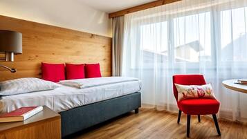 A modern hotel room with a wooden headboard, a bed with white bedding, a red chair, and a bedside table with a book.