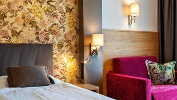 Una habitación de hotel con una cama, un sillón rojo, una lámpara de pared y papel tapiz con motivos florales.