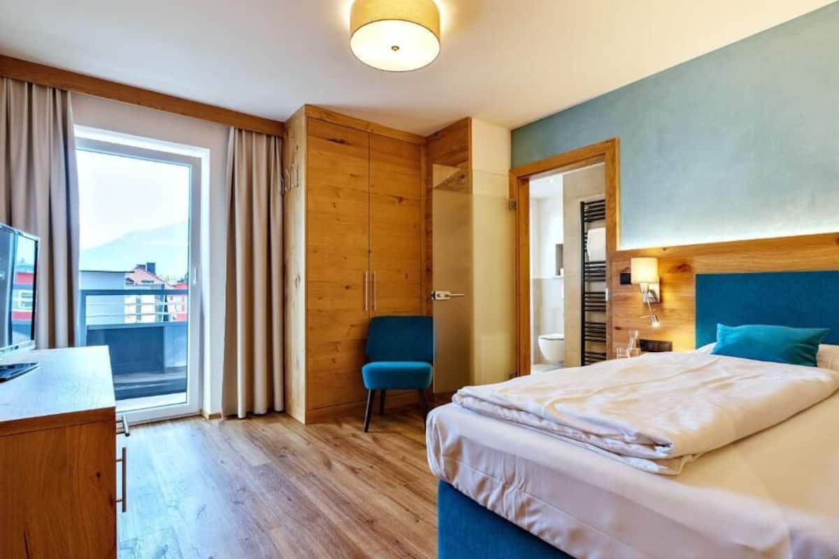 Habitación de hotel con cama, escritorio, silla, armario y vistas al exterior.