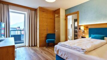 A hotel room with a bed, a desk, a chair, a wardrobe, and a view of the outside.