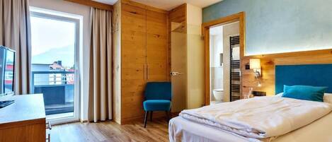 A hotel room with a bed, a desk, a chair, a wardrobe, and a view of the outside.