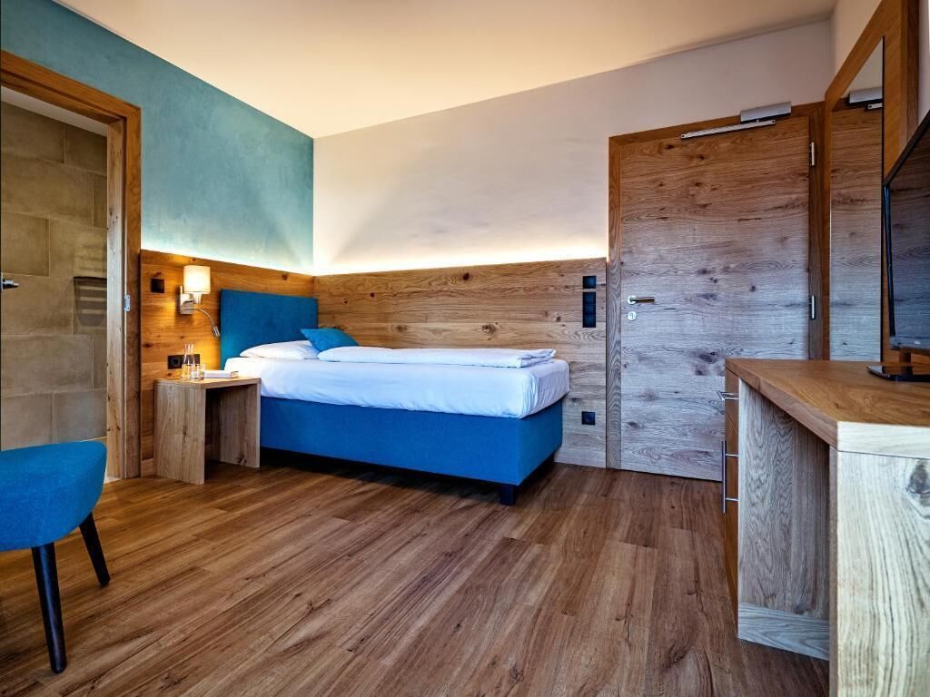 Um quarto moderno com cabeceira de madeira, cama com roupa de cama azul, mesa de cabeceira com abajur e guarda-roupa de madeira.