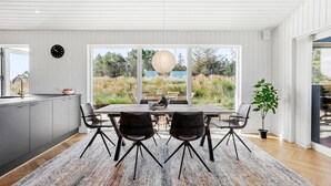 Une cuisine moderne dotée d’un grand îlot central, d’un coin repas avec une table et des chaises, et offrant une vue sur un jardin grâce à de grandes fenêtres.