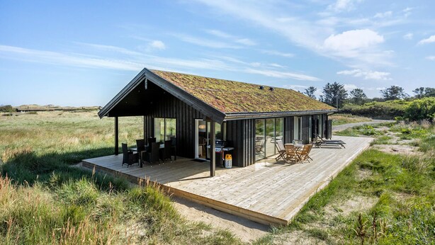 Une cabane moderne en bois, dotée d’un toit en pente, de grandes fenêtres en verre et d’une terrasse aménagée avec du mobilier d’extérieur.