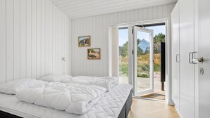 Une chambre avec un grand lit, une porte-fenêtre coulissante donnant sur une terrasse extérieure et deux tableaux encadrés accrochés au mur.