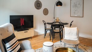 Una sala de estar moderna con un televisor de pantalla plana, una mesa de comedor con sillas, una lámpara y decoración en la pared.