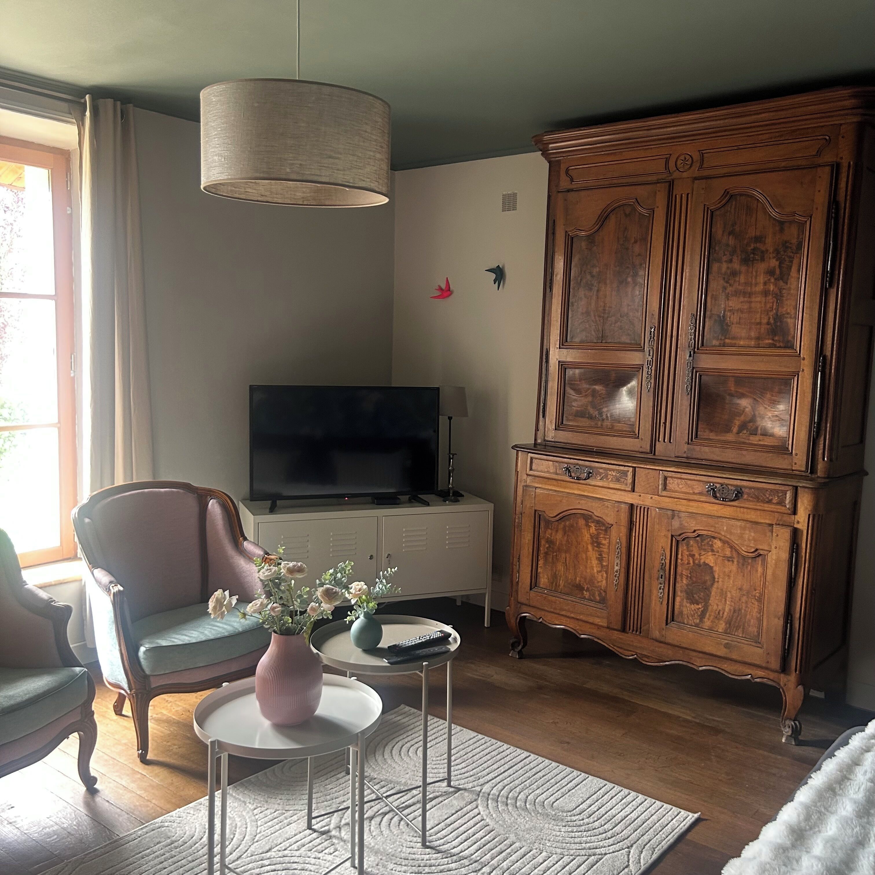 A living room with a television, a wooden cabinet, a chair, and a small table with a vase.