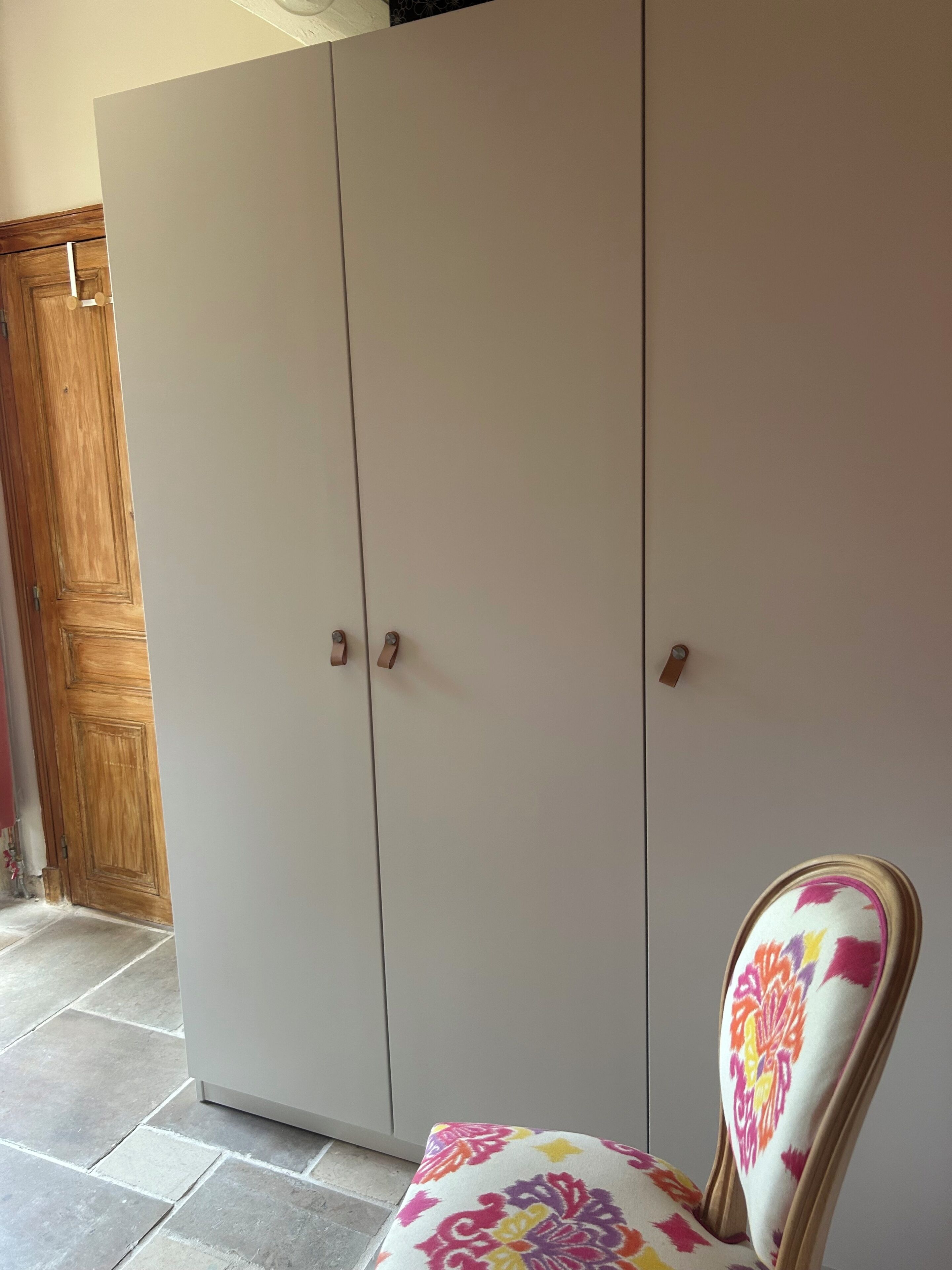 Een kamer met een grote kast, een houten deur en een gestreept stoel.