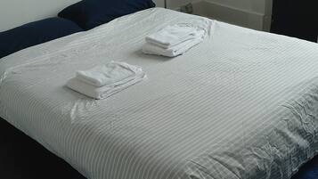 Una cama bien tendida con sábanas blancas y dos toallas dobladas, un cabecero azul oscuro y un cuadro en la pared.