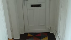 Eine weiße Tür mit Briefschlitz, ein dunkler Holzboden und ein farbenfroher, geometrischer Teppich im Eingangsbereich.