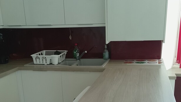 Eine Küche mit weißen Schränken, einer Holz Arbeitsplatte und einer dunkel gefliesten Spritzschutzwand.