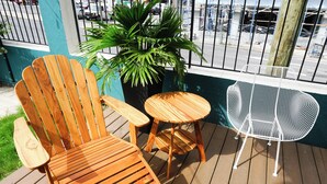 Eine Holzterrasse mit einem Holzstuhl, einem kleinen runden Tisch und einem weißen Metallstuhl.