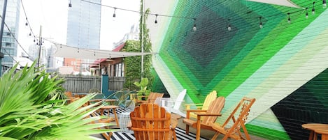 Un espace extérieur aménagé avec des chaises et des tables en bois, un mur végétal et des guirlandes lumineuses.