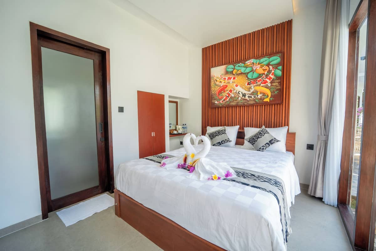 Een hotelkamer met een groot bed, een houten hoofdeinde, een aan de muur bevestigd schilderij en een schuifglazen deur.
