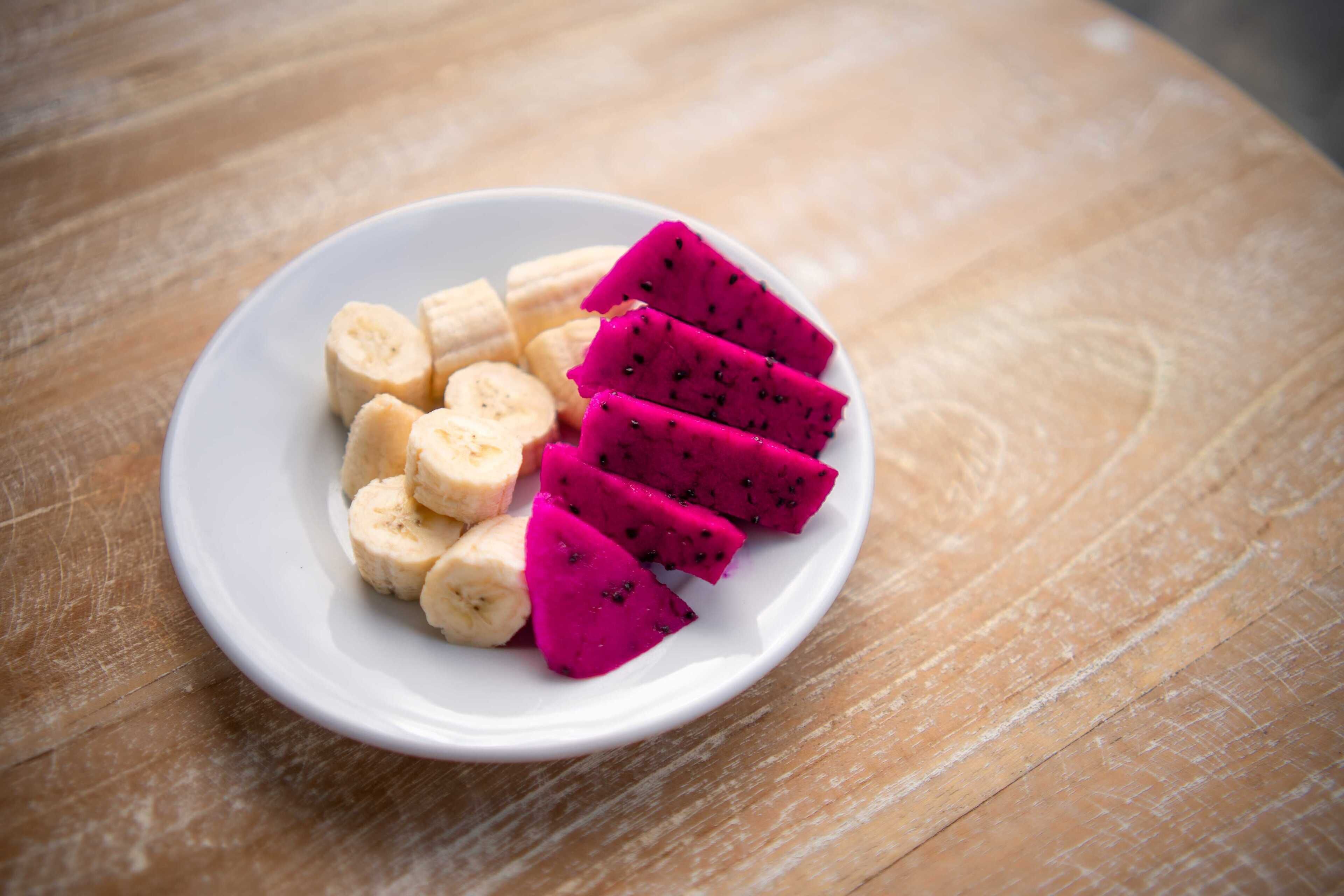 A white plate with sliced dragon fruit and bananas on a wooden surface.