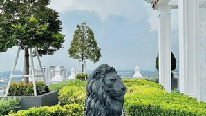 Una estatua de león en un jardín ajardinado con vista a edificios al fondo.
