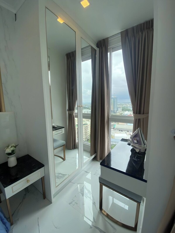 Una habitación de hotel moderna con un espejo grande, un escritorio con un florero, una silla y vista a la ciudad a través de la ventana.