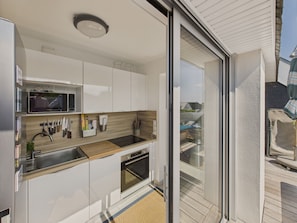 A modern kitchen with white cabinets, a stainless steel sink, a microwave, and an oven.