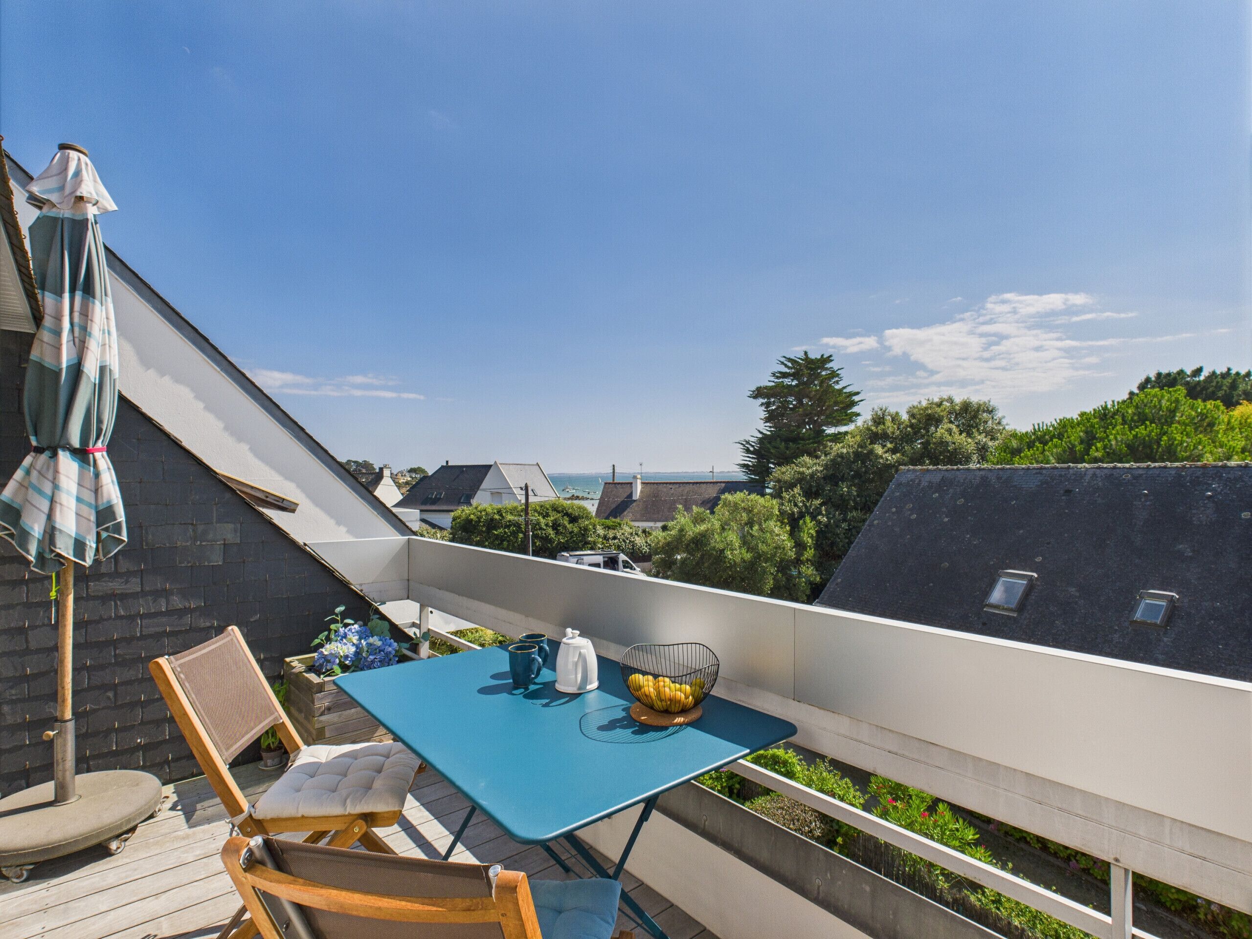 Ein Balkon mit einem blauen Tisch, zwei Stühlen, einer kleinen Pflanze und einer Obstschale.