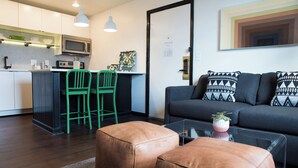 A modern kitchen with a microwave, green chairs, and a dining area. There is a sofa with patterned cushions and a coffee table with a plant. - Sleeps 8 | 4 SoBro Suites w/ Kitchens, Walk to Broadway – by AvantStay (Nashville)