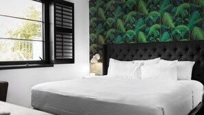 A neatly made bed with white linens in a room with a large window and a wall with a tropical leaf pattern. - Sleeps 8 | 4 SoBro Suites w/ Kitchens, Walk to Broadway – by AvantStay (Nashville)