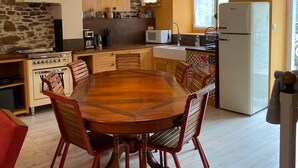 A kitchen with a central island, a dining table with chairs, a stove, a refrigerator, and pendant lighting.