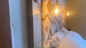 A bed with white bedding, a wooden headboard, and a wall-mounted shelf with a light fixture.