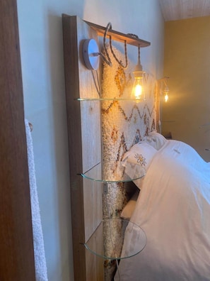 A bed with white bedding, a wooden headboard, and a wall-mounted shelf with a light fixture.