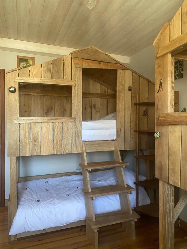 A wooden bunk bed with a ladder, a small shelf, and a door with a bird decoration.